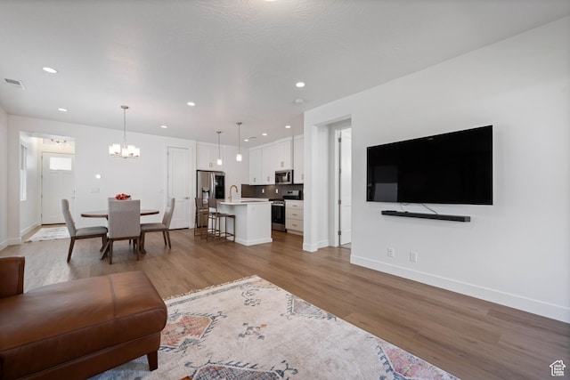 living area with visible vents, recessed lighting, a chandelier, light wood finished floors, and baseboards