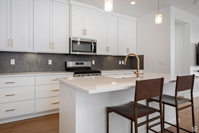 kitchen featuring a sink, a kitchen bar, wood finished floors, stainless steel appliances, and backsplash