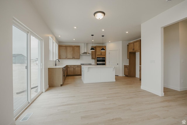 kitchen with wall chimney exhaust hood, light wood-type flooring, brown cabinetry, light countertops, and double oven