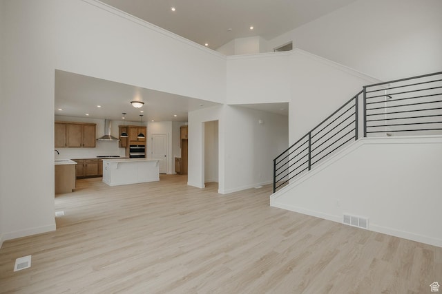 unfurnished living room with stairs, light wood-style floors, baseboards, a towering ceiling, and recessed lighting