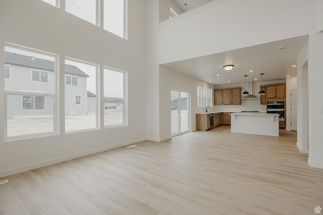 unfurnished living room with light wood-type flooring, a sink, baseboards, and a towering ceiling