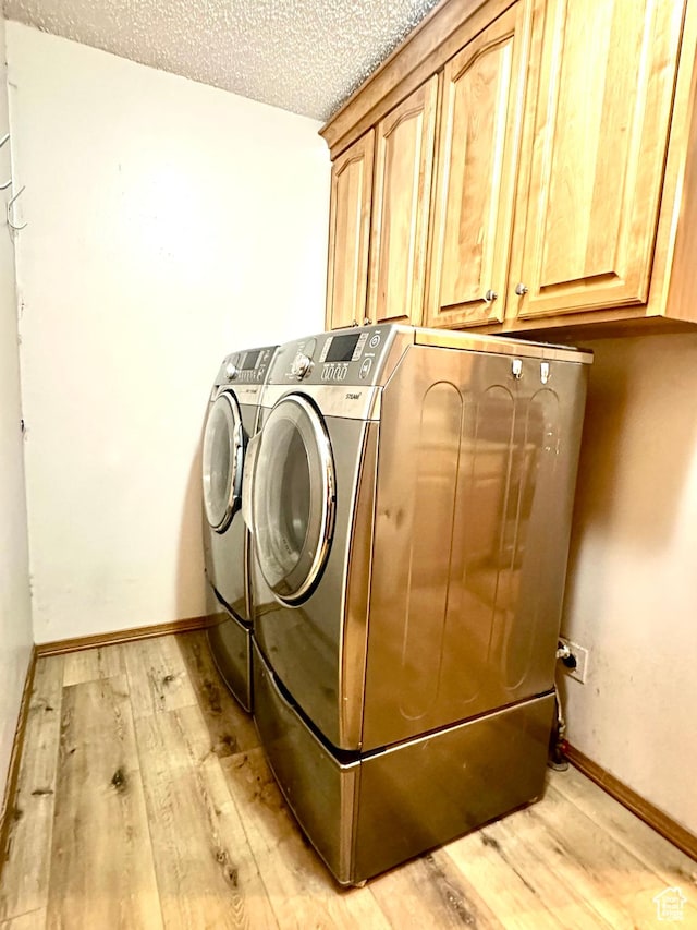 laundry area with cabinet space, independent washer and dryer, light wood-style flooring, a textured ceiling, and baseboards