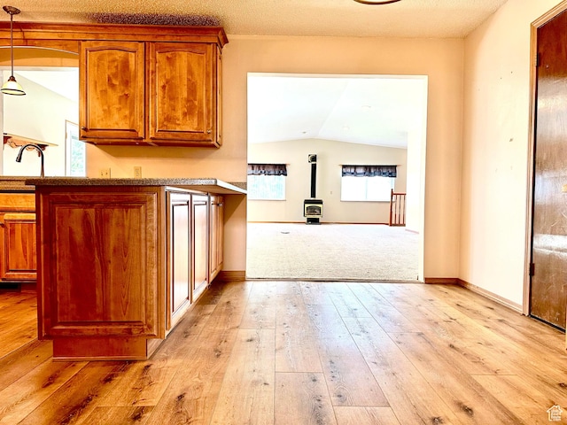 kitchen with a wood stove, brown cabinets, vaulted ceiling, light wood-style floors, and pendant lighting
