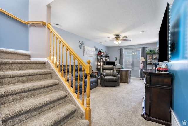 carpeted living room featuring stairs, visible vents, and a ceiling fan