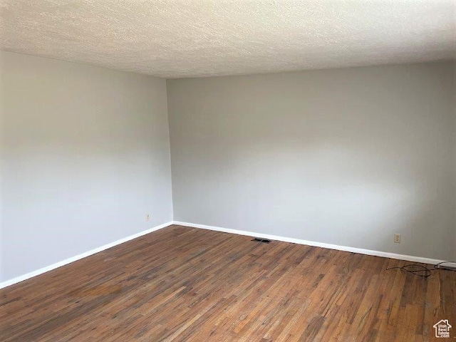 empty room with a textured ceiling, baseboards, dark wood-style floors, and visible vents