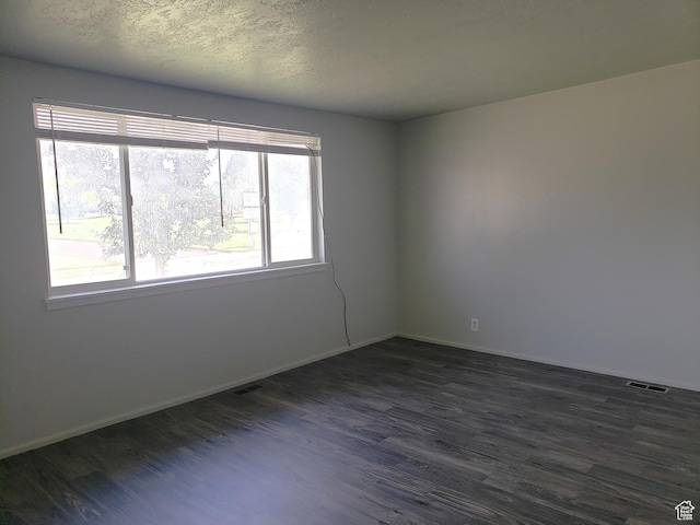 spare room featuring dark wood-type flooring, visible vents, and baseboards