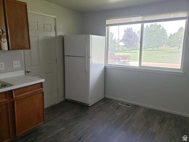 kitchen with dark wood-type flooring, freestanding refrigerator, light countertops, and a wealth of natural light