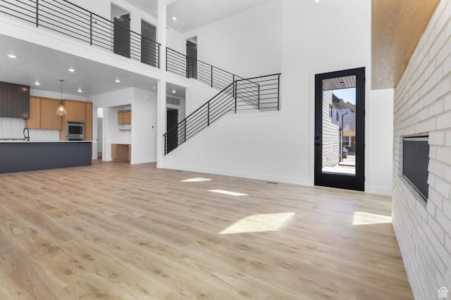 4125 N Maple Blvd W Unit 119, Lehi, UT 84043 - unfurnished living room with a towering ceiling, a fireplace, light wood-style flooring, baseboards, and stairs