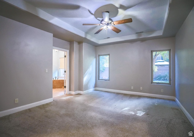 carpeted spare room with a raised ceiling, baseboards, and a ceiling fan