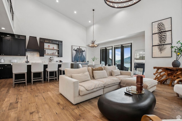 living room featuring indoor wet bar, a chandelier, light wood-style floors, recessed lighting, and high vaulted ceiling