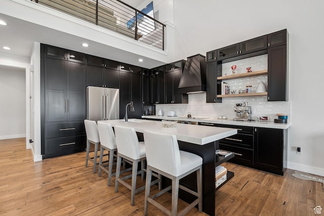 kitchen featuring light countertops, a sink, custom range hood, baseboards, and black electric cooktop