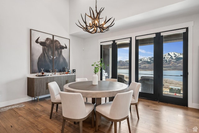 dining area with a water view, wood-type flooring, baseboards, and an inviting chandelier