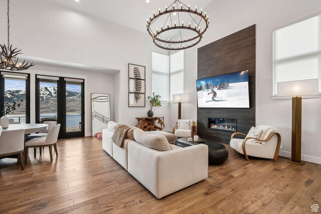 living area with a glass covered fireplace, wood-type flooring, a notable chandelier, and a high ceiling