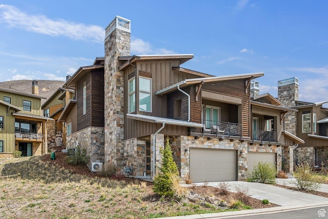contemporary home with stone siding, a garage, a chimney, board and batten siding, and concrete driveway