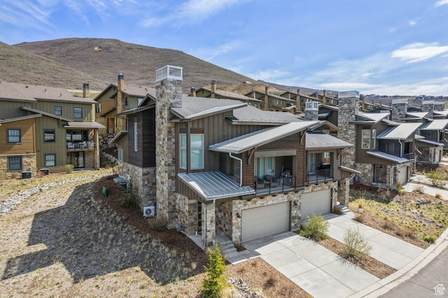 exterior space featuring stone siding, metal roof, a garage, concrete driveway, and a residential view