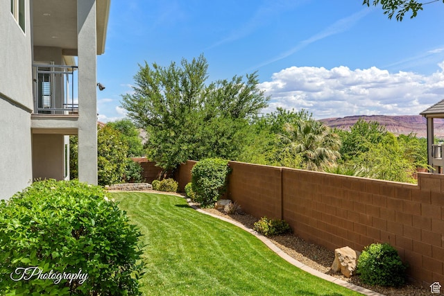 view of yard featuring a mountain view, a fenced backyard, and a balcony
