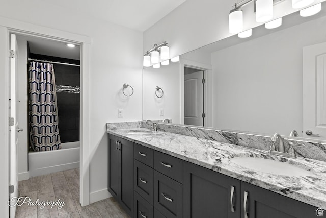 bathroom with double vanity, a sink, shower / bathtub combination with curtain, and wood finished floors