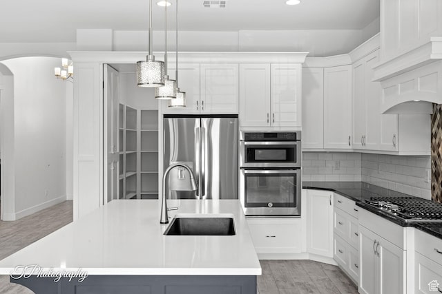 kitchen featuring tasteful backsplash, arched walkways, a sink, light wood finished floors, and stainless steel appliances