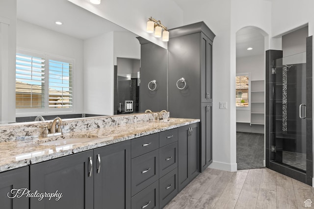 full bathroom with a shower stall, double vanity, a sink, and wood finished floors