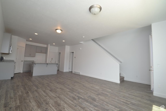 unfurnished living room featuring stairs, visible vents, baseboards, and dark wood-style floors