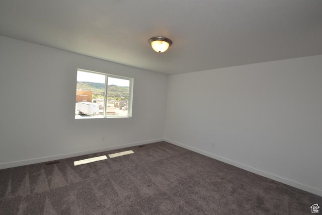 spare room featuring dark carpet, baseboards, and visible vents