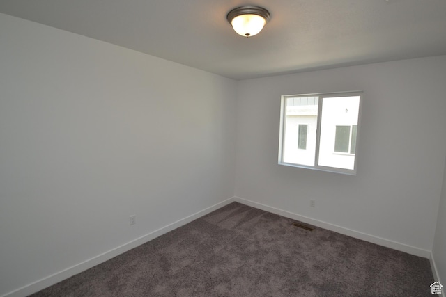 spare room with dark carpet, baseboards, and visible vents