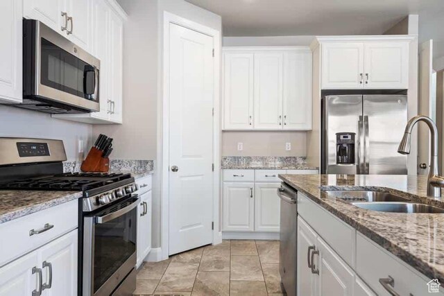 kitchen with a sink, white cabinetry, light stone countertops, and stainless steel appliances