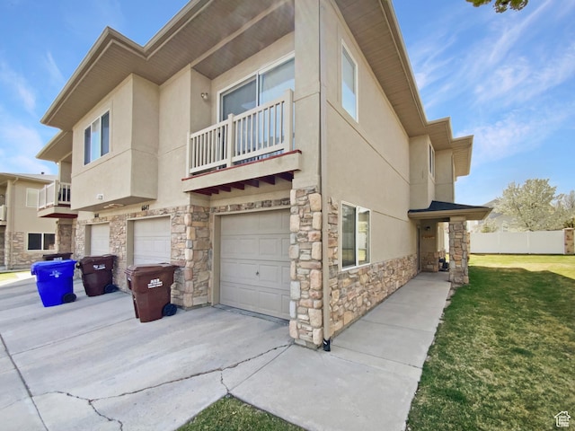 view of property exterior with a yard, an attached garage, stone siding, a balcony, and stucco siding