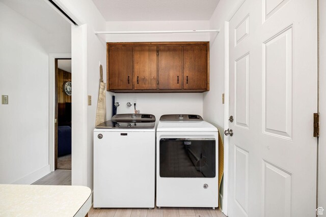 laundry area featuring cabinet space, light wood-style flooring, washing machine and dryer, and baseboards