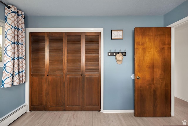 unfurnished bedroom with a closet, a baseboard radiator, light wood finished floors, and baseboards