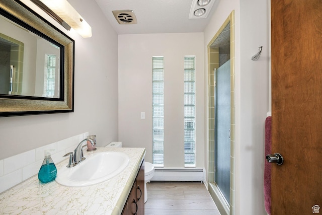 bathroom featuring toilet, vanity, wood finished floors, a baseboard heating unit, and a shower with shower door