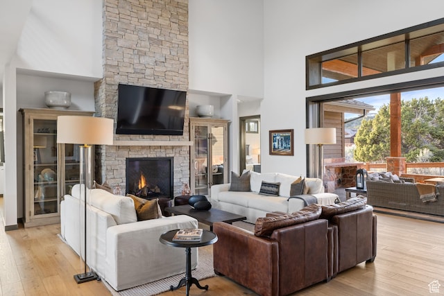 living room featuring a stone fireplace, light wood-type flooring, and a high ceiling