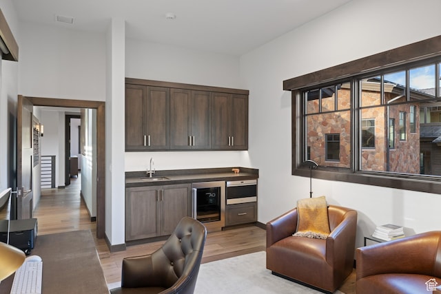 home office with indoor wet bar, light wood-style floors, a sink, and wine cooler