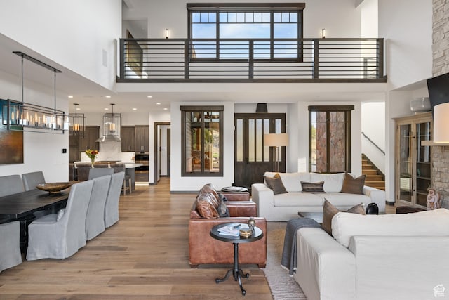 living room with light wood-style flooring, a towering ceiling, plenty of natural light, and stairway
