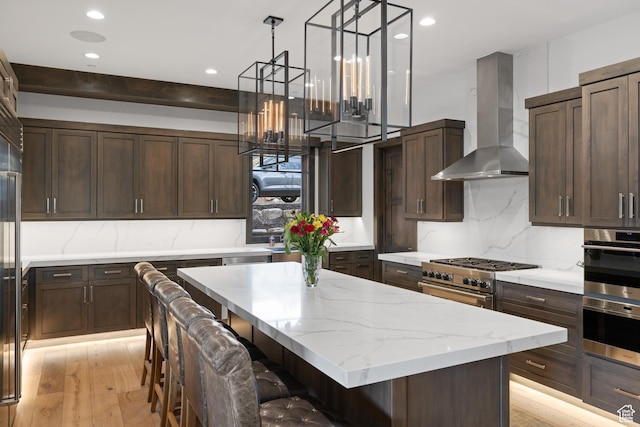 kitchen featuring recessed lighting, wall chimney exhaust hood, dark brown cabinetry, and stainless steel appliances