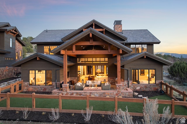 back of house featuring an outdoor living space, a fenced backyard, a patio area, stone siding, and a chimney