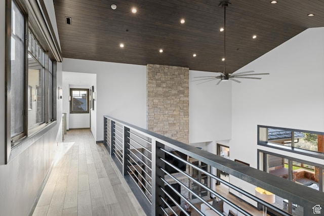 hallway with light wood-style flooring, wooden ceiling, high vaulted ceiling, and an upstairs landing