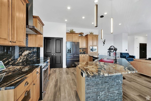 kitchen featuring dark stone countertops, wall chimney exhaust hood, a sink, open floor plan, and stainless steel appliances