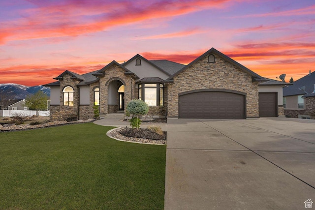 french country home with a garage, a front yard, driveway, and stone siding