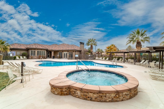 community pool with a patio, fence, and a hot tub