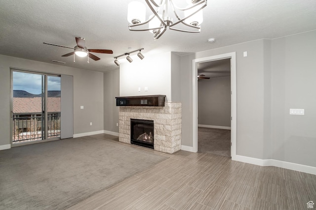 unfurnished living room featuring a fireplace, ceiling fan with notable chandelier, baseboards, and a textured ceiling
