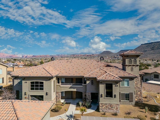 mediterranean / spanish-style home with a balcony, stucco siding, a mountain view, stone siding, and a tile roof