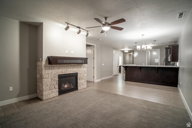 unfurnished living room featuring a fireplace, visible vents, ceiling fan with notable chandelier, and baseboards