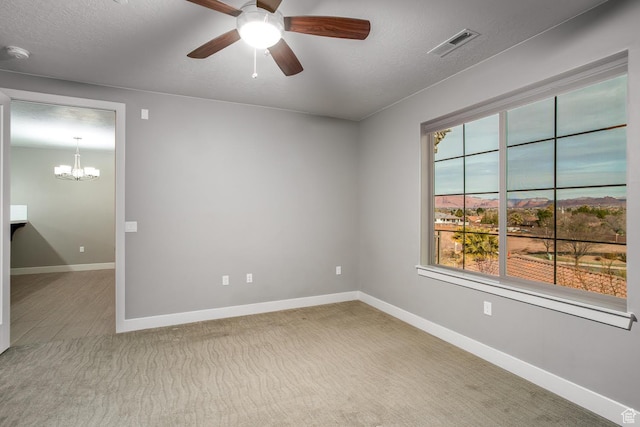 carpeted spare room featuring visible vents, baseboards, a textured ceiling, and ceiling fan with notable chandelier