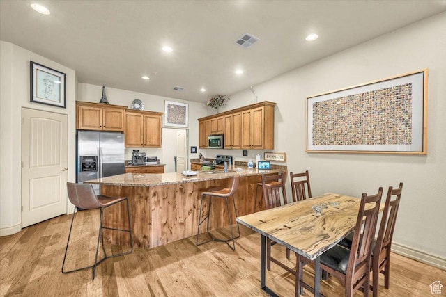 kitchen featuring light wood-style floors, a peninsula, brown cabinets, recessed lighting, and stainless steel appliances