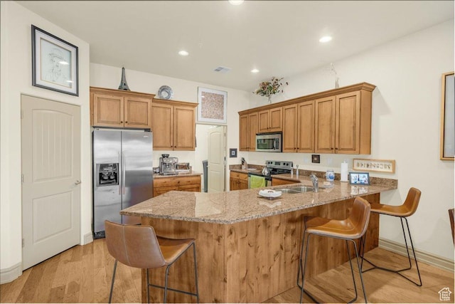 kitchen with visible vents, a sink, appliances with stainless steel finishes, a peninsula, and light stone countertops