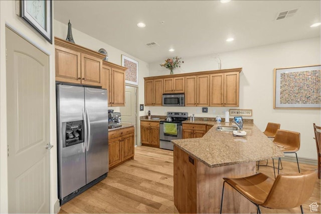 kitchen featuring a sink, appliances with stainless steel finishes, a kitchen breakfast bar, a peninsula, and light wood finished floors