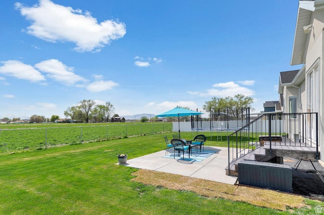 view of yard with a trampoline, a patio, a fenced backyard, and a rural view