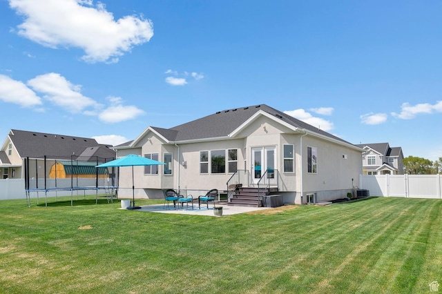 back of property with a trampoline, cooling unit, a patio area, a fenced backyard, and a lawn
