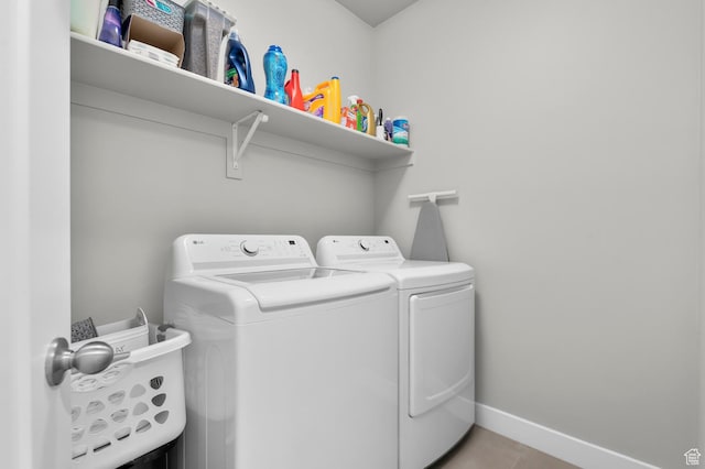 clothes washing area with laundry area, washing machine and clothes dryer, baseboards, and light tile patterned floors